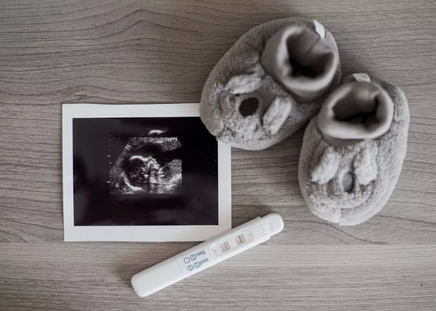 A pregnancy test and baby shoes on a wooden table