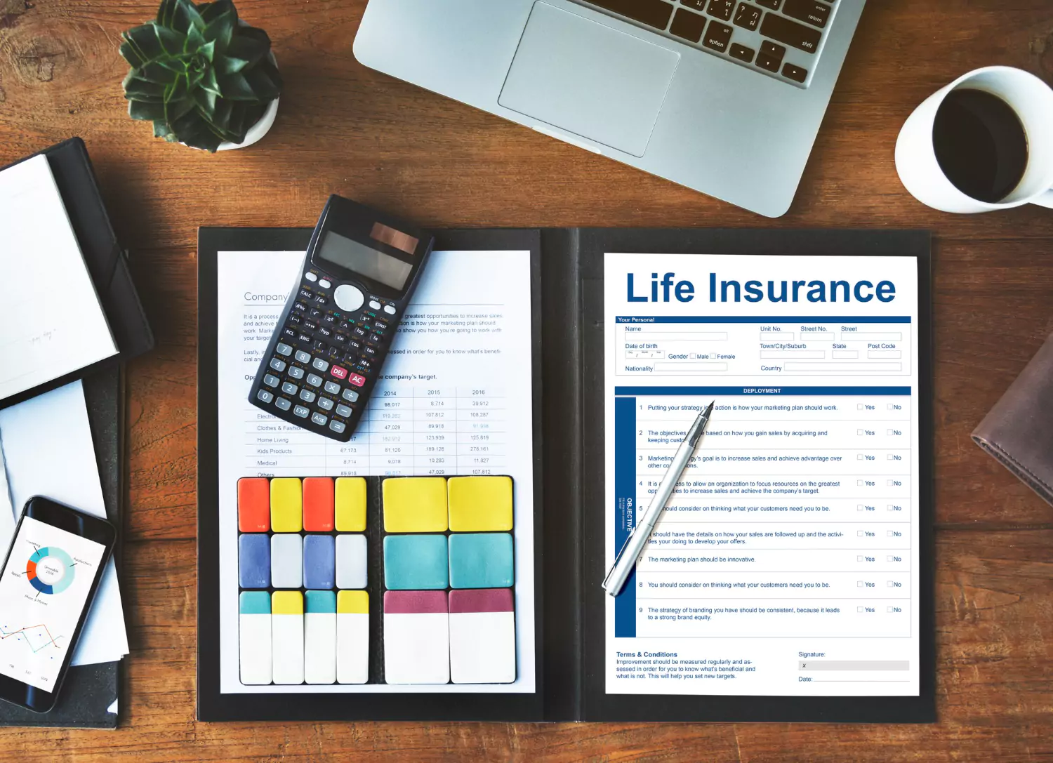 A desk with a laptop, phone, and life insurance documents.